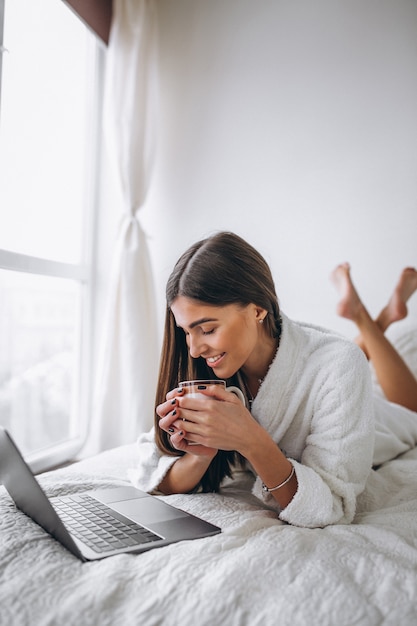 若い女性がベッドの中でコンピューターに取り組んで