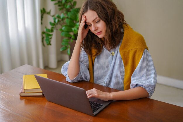 Young woman working at freelance home office, feels tired after work