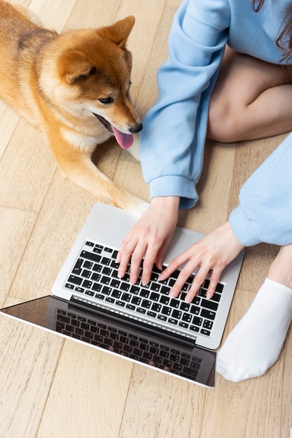 Foto gratuita giovane donna che lavora al suo computer portatile accanto al suo cane