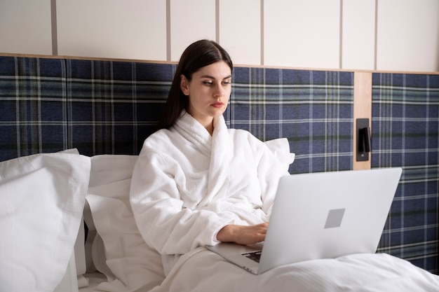 Foto gratuita giovane donna che lavora al suo computer portatile mentre è seduta sul letto in una camera d'albergo