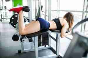 Free photo young woman working her quads at machine press in the gym