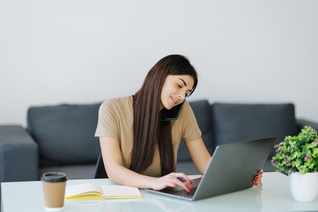 Young woman working on laptop smiling talking on phone sun coming through window