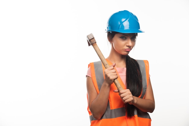 Young woman working with hammer on white wall 