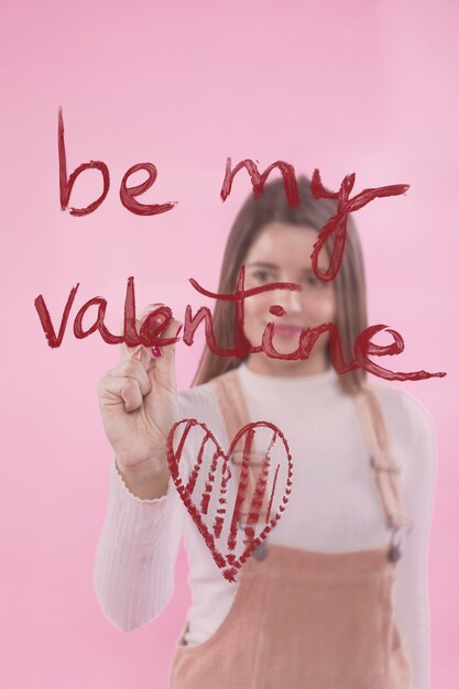 Young woman writing Be my valentine on glass with lipstick