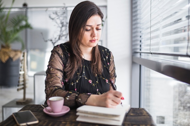 Young woman writing in diary at restaurant