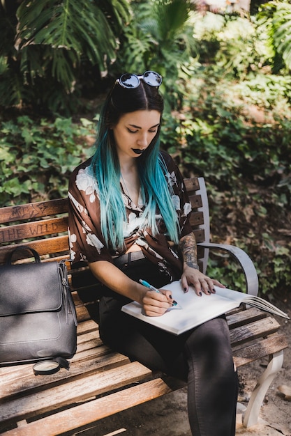 Foto gratuita scrittura della giovane donna sul taccuino che si siede sulla panchina nel parco