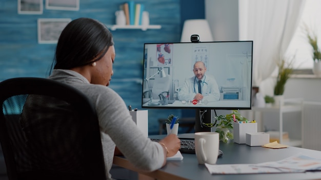Young woman writing respiratory sickness treatment on notebook, discussing pills and treatment during online healthcare videocall