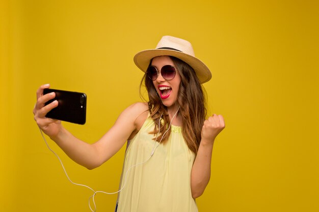 Young woman in yellow dress with hat and sunglasses, watching video