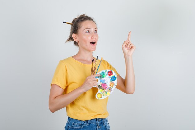 Young woman in yellow pointing up finger with art tools