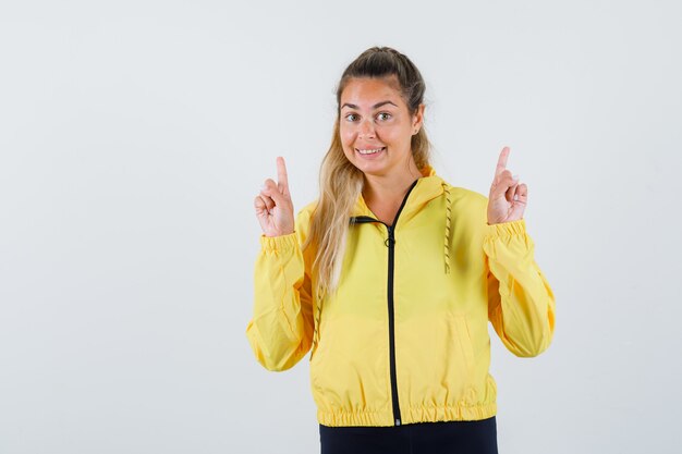 Young woman in yellow raincoat pointing up and looking pleased