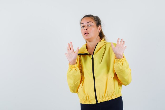 Young woman in yellow raincoat raising hands for rejecting something and looking reluctant