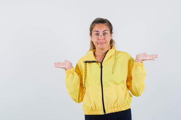 Young woman in yellow raincoat showing helpless gesture