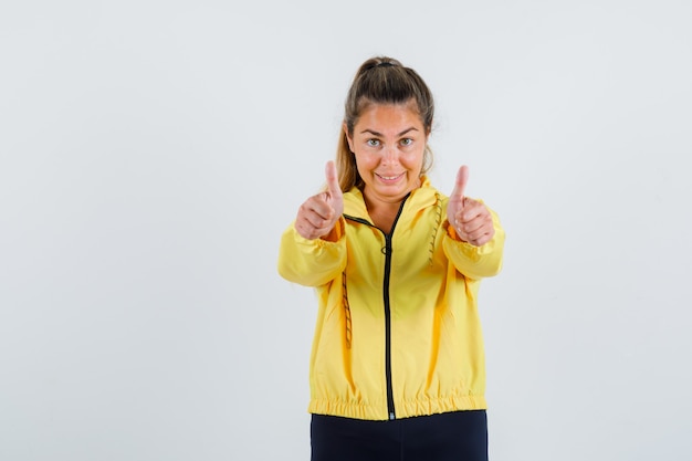 Young woman in yellow raincoat showing thumb up and looking glad