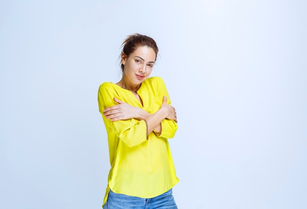 腕を組んで寒い黄色のシャツを着た若い女性