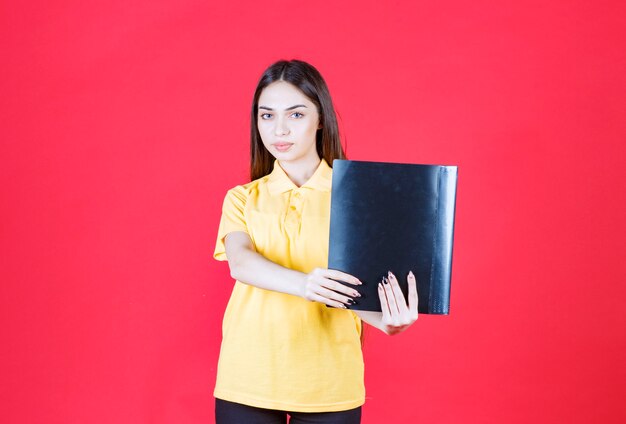 黒いフォルダーを保持している黄色いシャツの若い女性