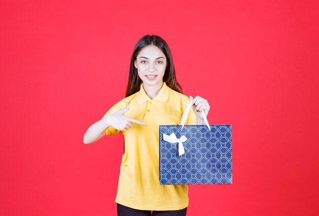 Молодая женщина в желтой рубашке держит синюю сумку для покупок