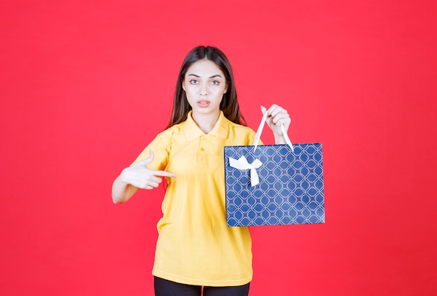 Молодая женщина в желтой рубашке держит синюю сумку для покупок
