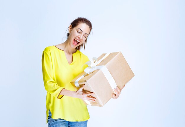 Young woman in yellow shirt holding a cardboard gift box and screaming from happiness