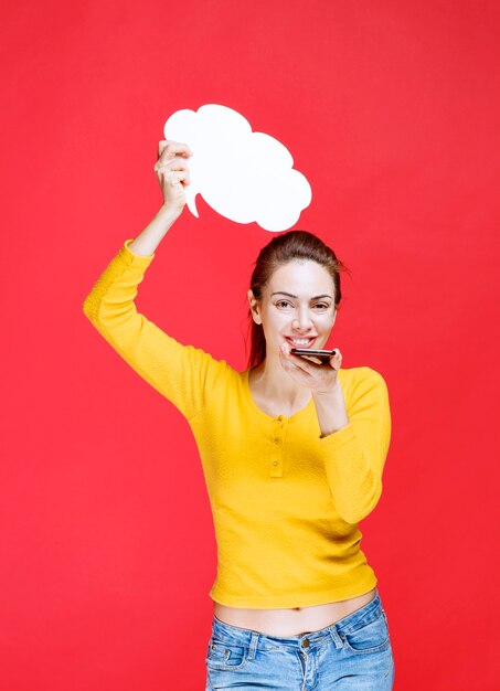 Young woman in yellow shirt holding a cloud shape info board and sending an audio message