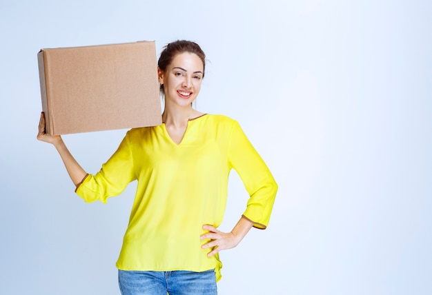 Young woman in yellow shirt holding her cardboard cargo box and feeling happy