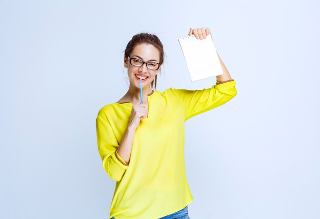Молодая женщина в желтой рубашке держит экзаменационный лист и думает, держа ручку