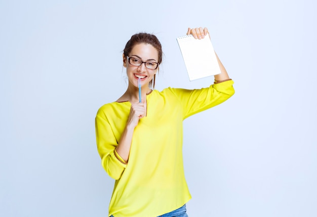 Young woman in yellow shirt holding her exam sheet and thinking while holding a pen