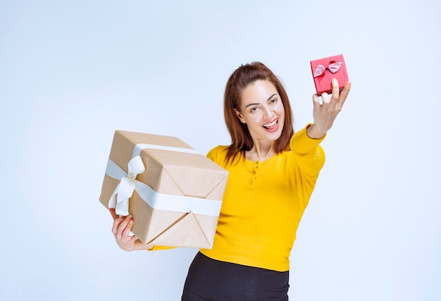 Young woman in yellow shirt holding a red and a cardboard gift boxes