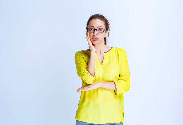 Young woman in yellow shirt looks thoughtful