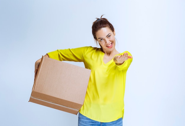 Free photo young woman in yellow shirt offering a cardboard box