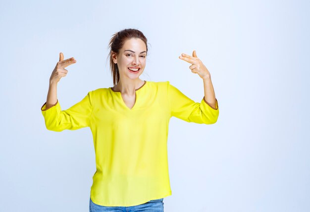 Young woman in yellow shirt pointing at herself