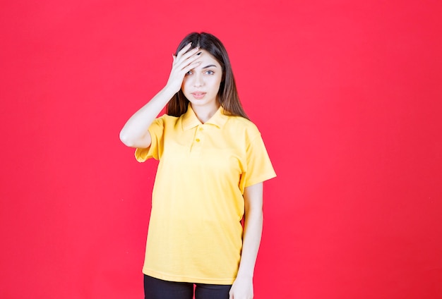 Young woman in yellow shirt standing on red wall and looks tired and sleepy