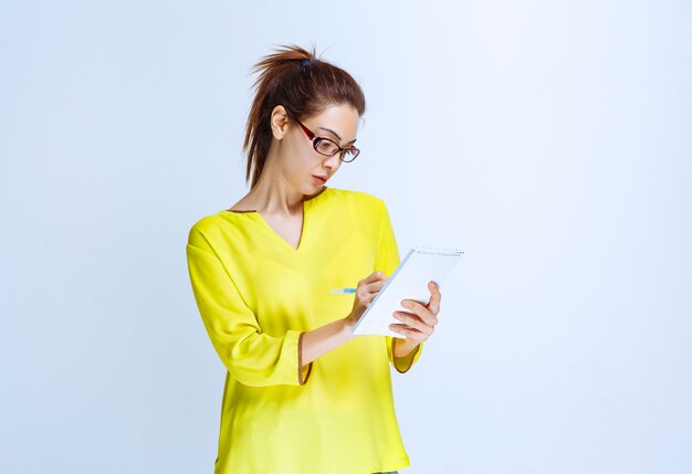 Young woman in yellow shirt taking her notes while the professor is speaking