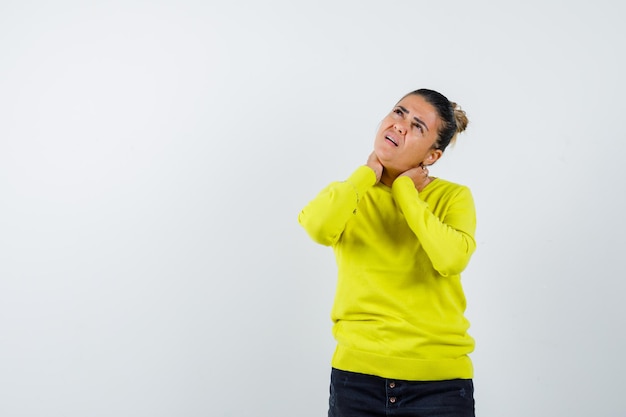 Young woman in yellow sweater and black pants having neck pain and looking harried