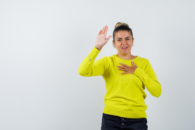 Young woman in yellow sweater and black pants resting hands and showing stop sign and looking happy