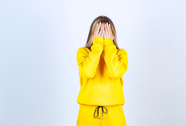 白い壁に顔を覆う黄色のスウェットスーツの若い女性