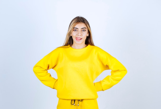 Young woman in yellow sweatsuit posing to camera over white wall