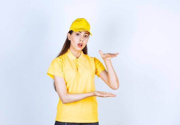 Young woman in yellow t-shirt and cap standing on white background.