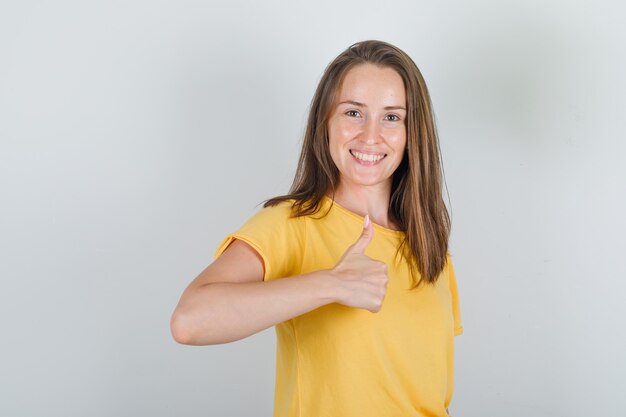 Young woman in yellow t-shirt showing thumb up and looking cheerful