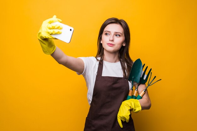 Young womang ardener take selfie on the phone while holding tools isolated