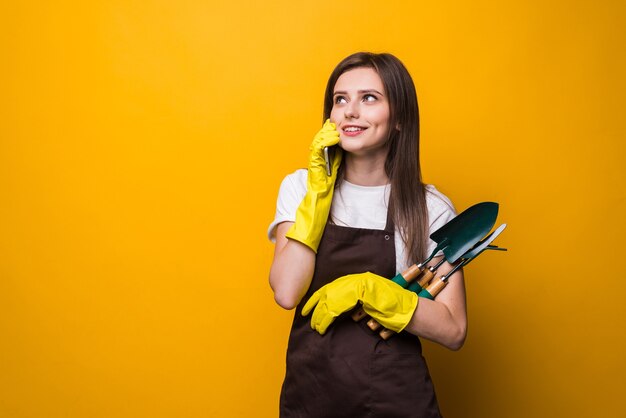 Young womang ardener talking on the phone while holding tools isolated