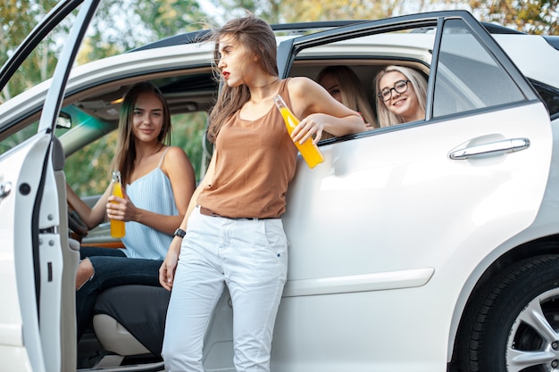 車の中で若い女性とジュースを飲んで、屋外で笑っています。ライフスタイル、旅行、冒険、女性の友情のコンセプト