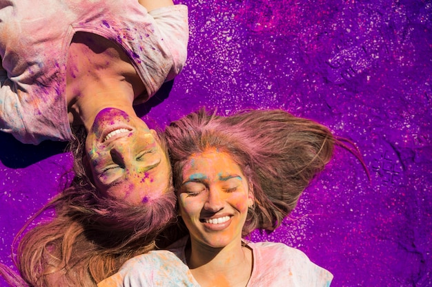 Young women covered with holi powder lying on purple color