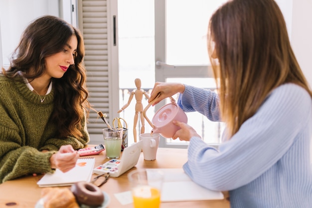 Young women drawing and pouring tea