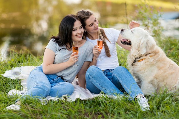 Young women drinking next to a dog outdoors