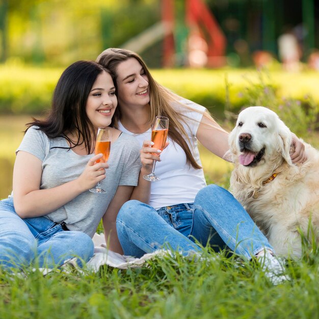 Young women drinking next to a dog outside