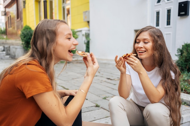 Young women eating pizza together outdoors