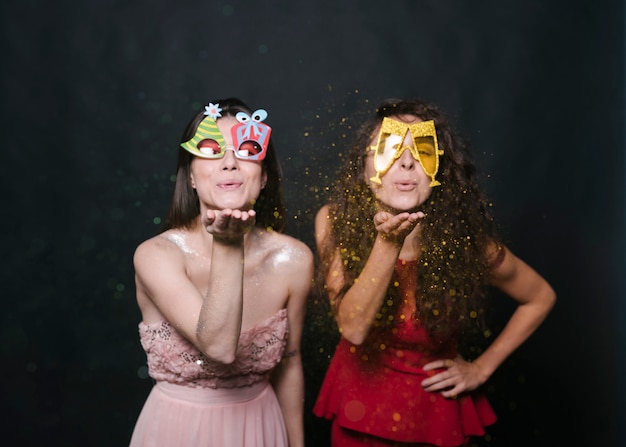 Free photo young women in funny eyeglasses blowing confetti from hands