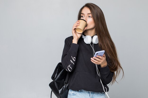 Молодые женщины держат смартфон и чашку кофе, изолированных на белой стене
