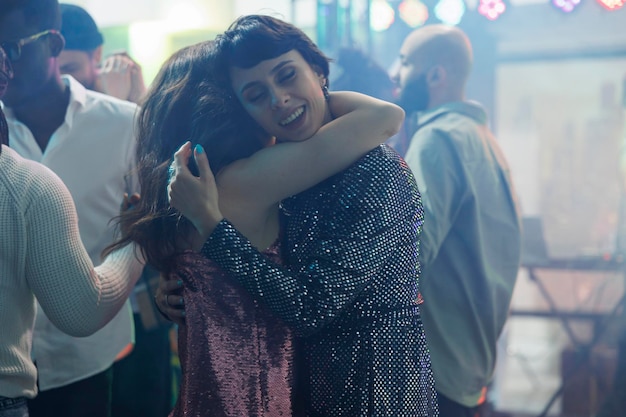 무료 사진 나이트클럽에서 디스코 파티에 참석하는 동안 젊은 여성들이 포옹하고 춤을 춥니다. 클럽의 디스코텍 행사에서 클럽 활동과 휴식을 취하는 동안 댄스 플로어에서 포옹하는 로맨틱한 여자 친구 커플