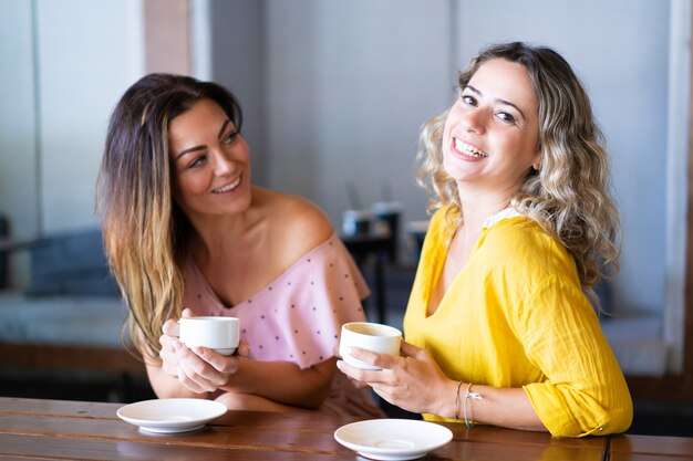 Young women laughing and drinking coffee in cafe